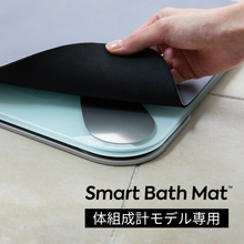 画像をギャラリービューアに読み込む, スマートバスマット体組成計モデル専用の、取り替え用ソフト珪藻土マットを手で持ち上げている様子。ライトブルーとブラックの二層構造。
